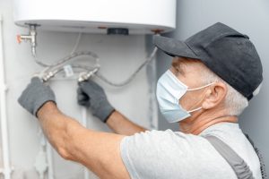Plumber man in medical mask installing boiler water heater in bathroom